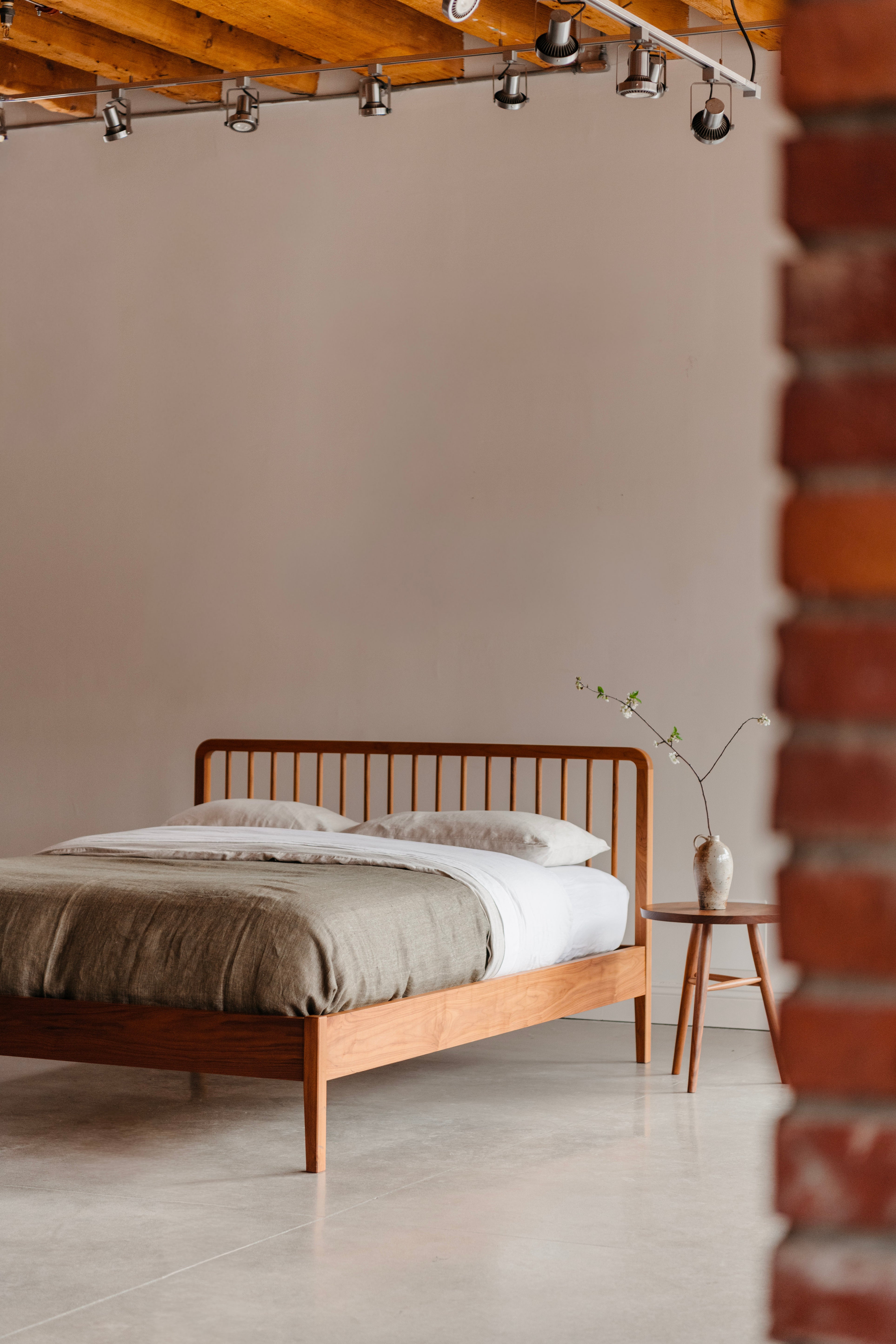 Walnut Dune Bed by Chilton Furniture with minimal decor, featuring a round side table and brick wall on the right.