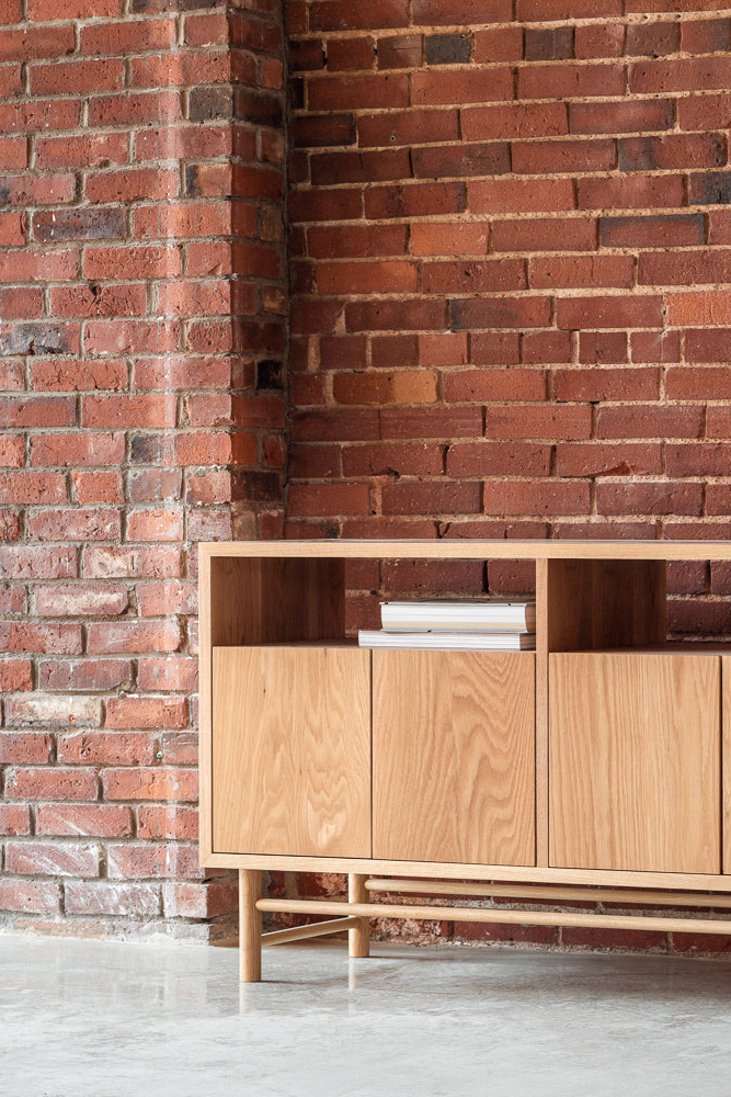 White oak Navarend Media Stand shown in white oak along brick wall