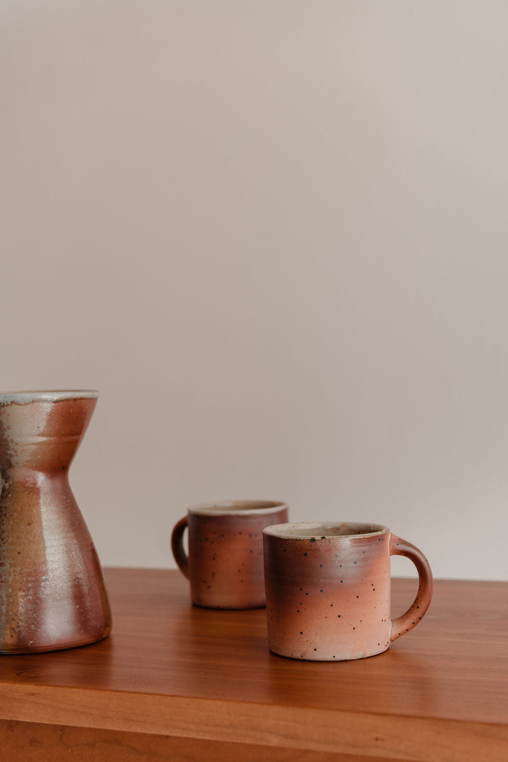 Two ceramic mugs and a pitcher on a wooden surface with a beige background