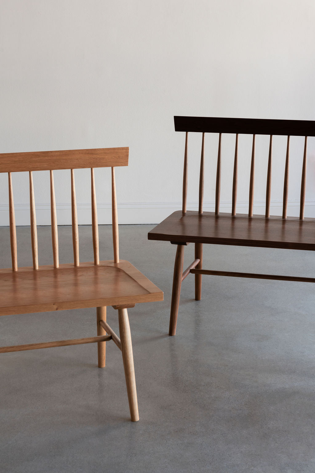 Image of the ends of two Broadside benches in cherry and walnut, angles toward each other in white room with cement floors