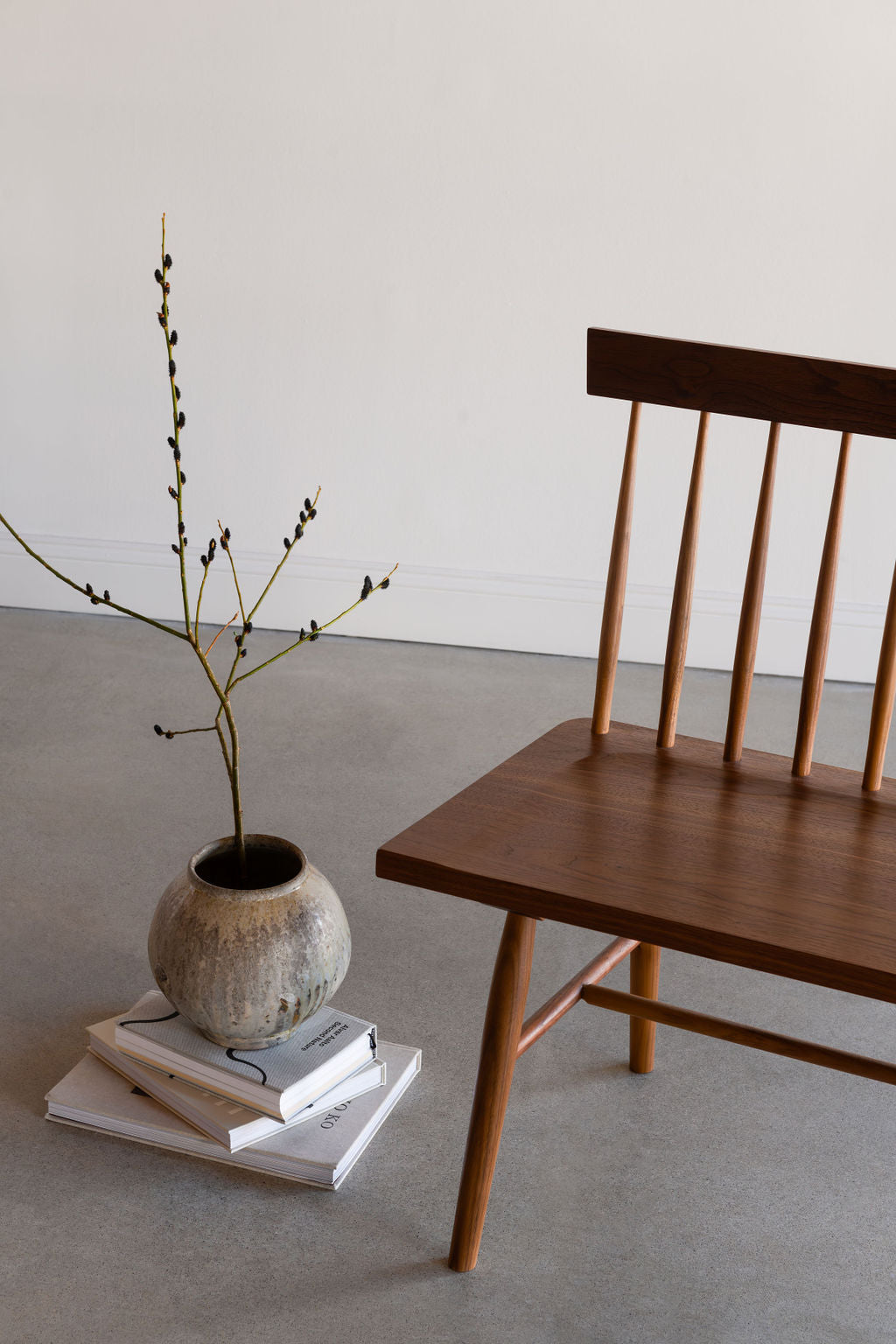 The traditional Shaker style spindle Broadside Bench with angular lines in walnut, styled with pottery and flora on books
