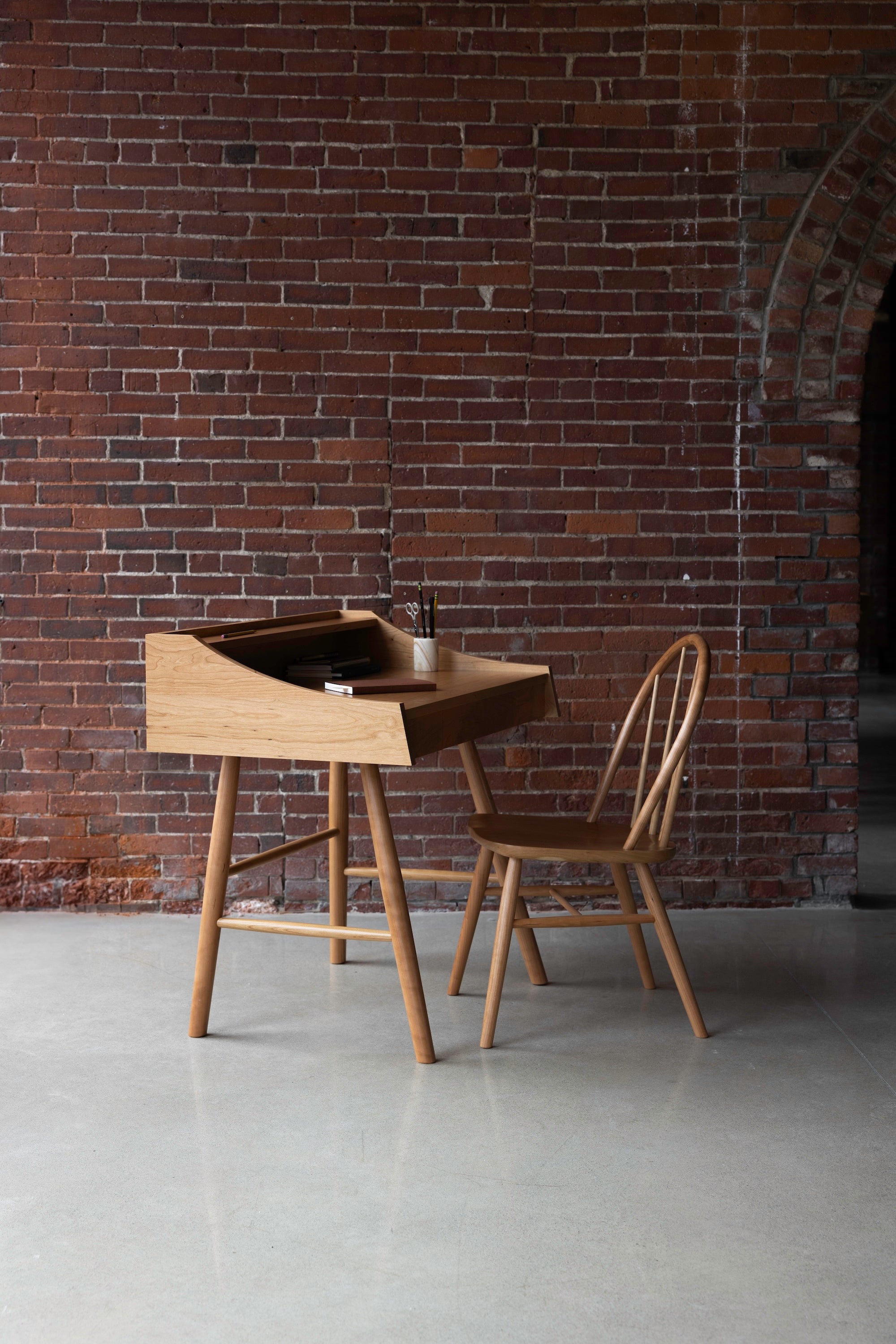 Hudson Desk and Chair made from solid cherry wood on a cement floor against a brick wall