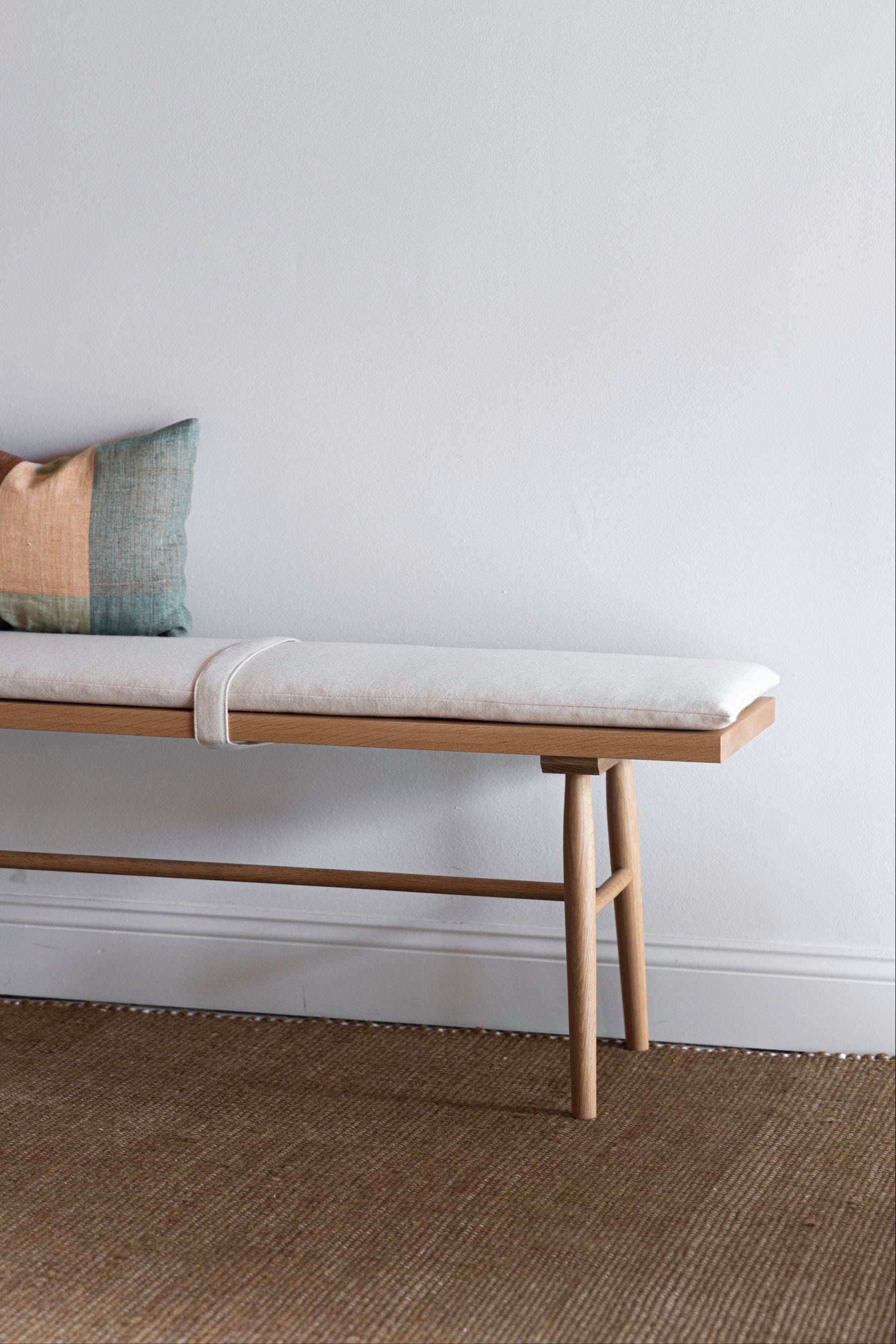 Chilton Furniture's Hudson Bench with a white fabric cushion and multicolor pillow against white wall on a jute rug