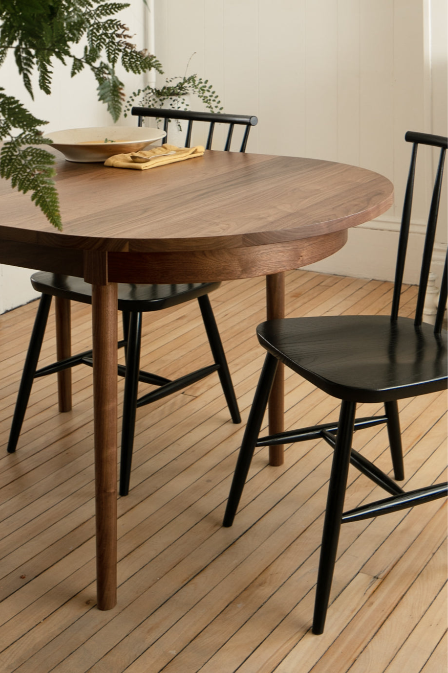 The Concord Chair painted black paired with the Highland Table, in a dining room with light wooden floors, set with a bowl of soup, and surrounded by ferns.