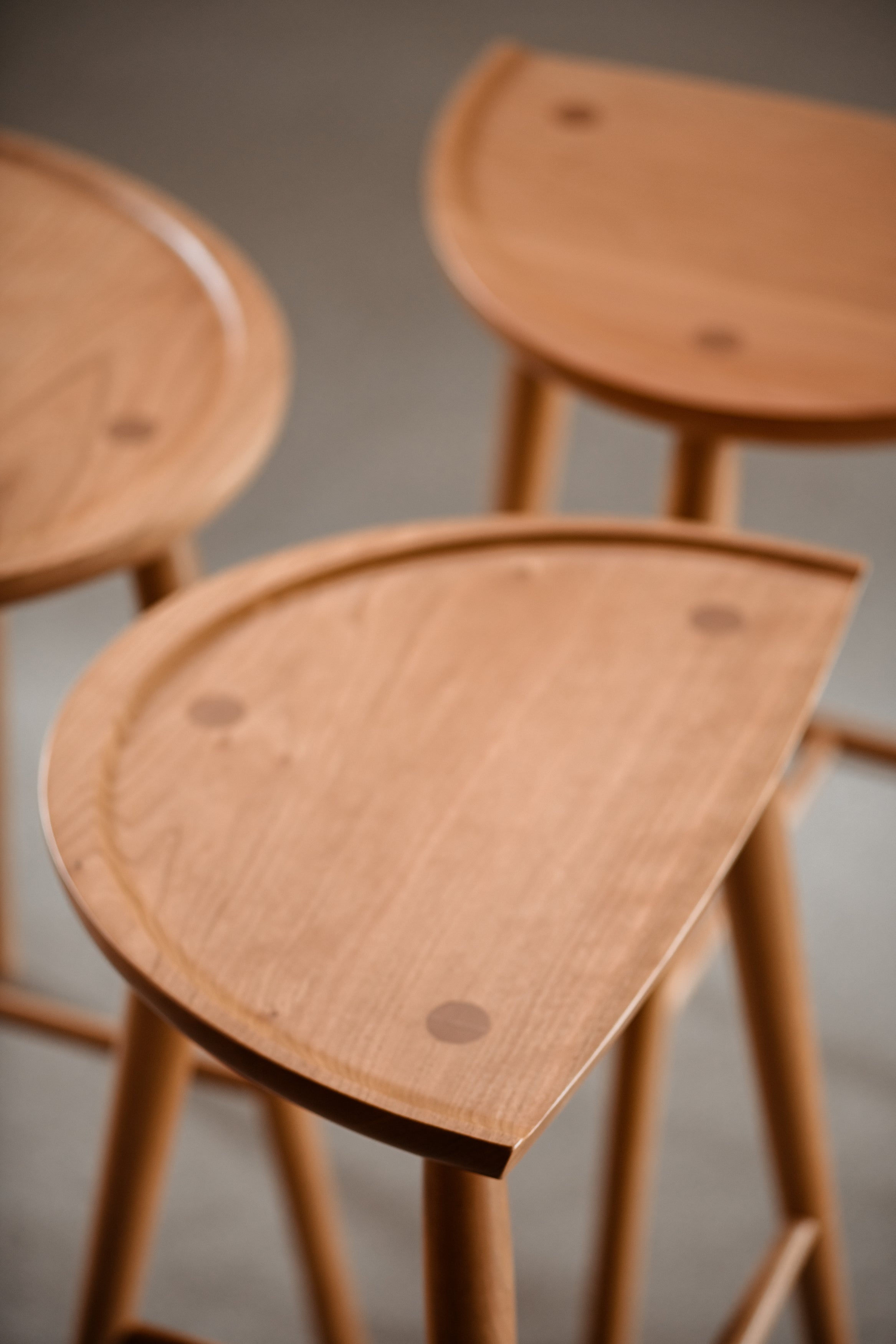 Three cherry Shaker Stools placed in a circle highlighting the curves of the seat and the traditional joinery.