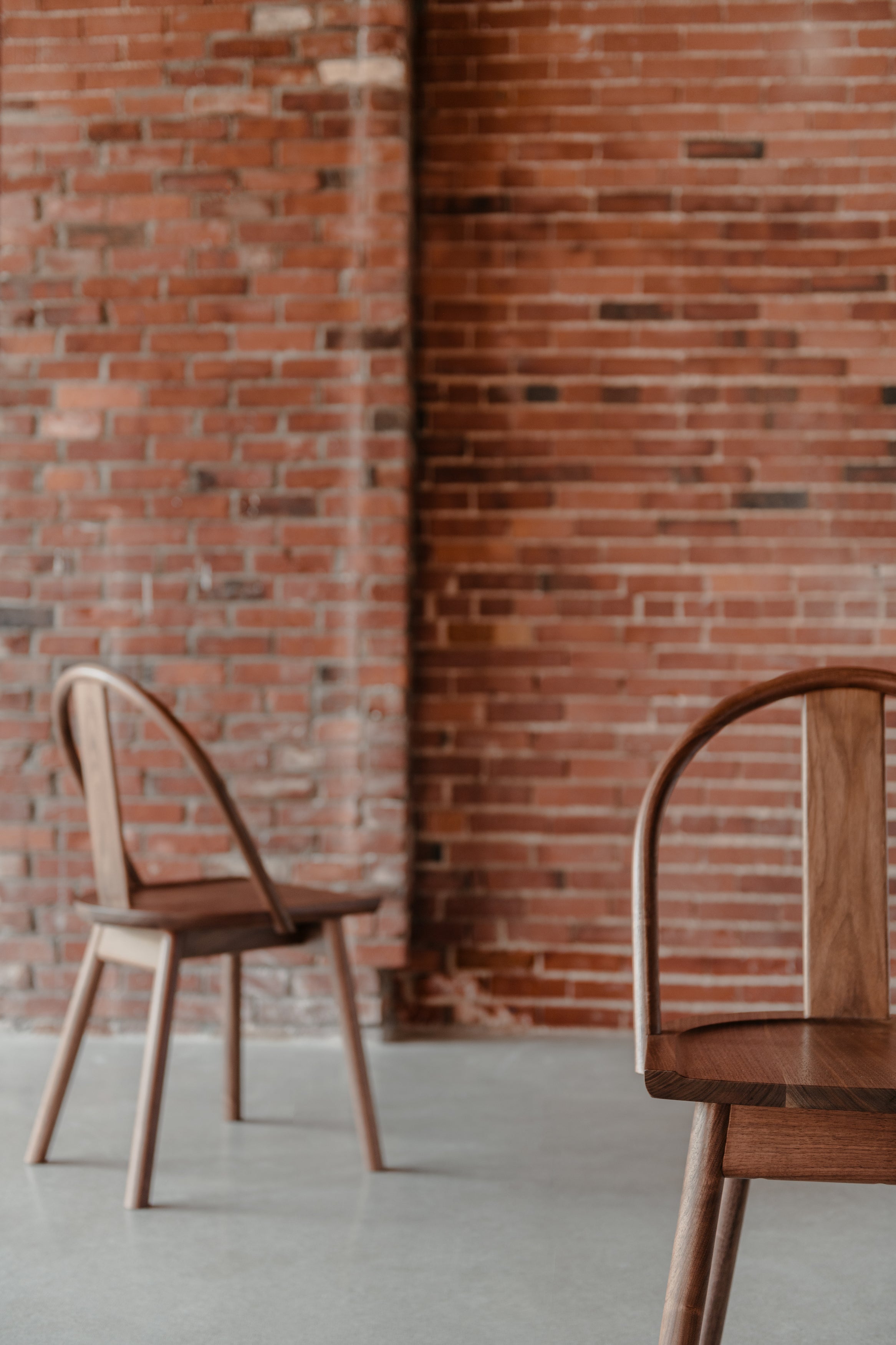 Two modern bowback Atlas Dining Chairs in walnut wood in front of a warm brick wall