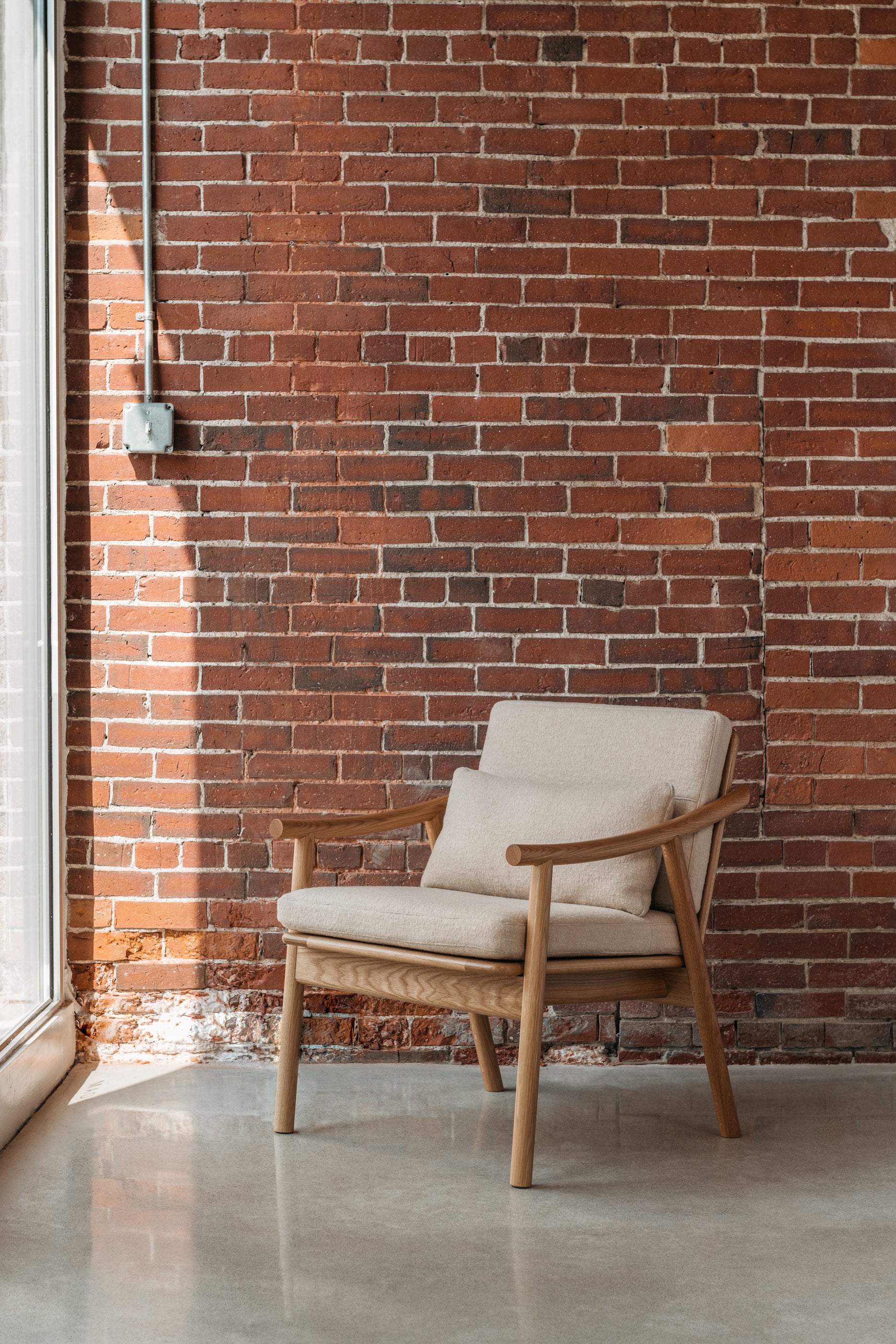 White Oak lounge chair in a bright window against a brick wall