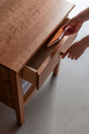 Placing a book into an open drawer on a wooden nightstand