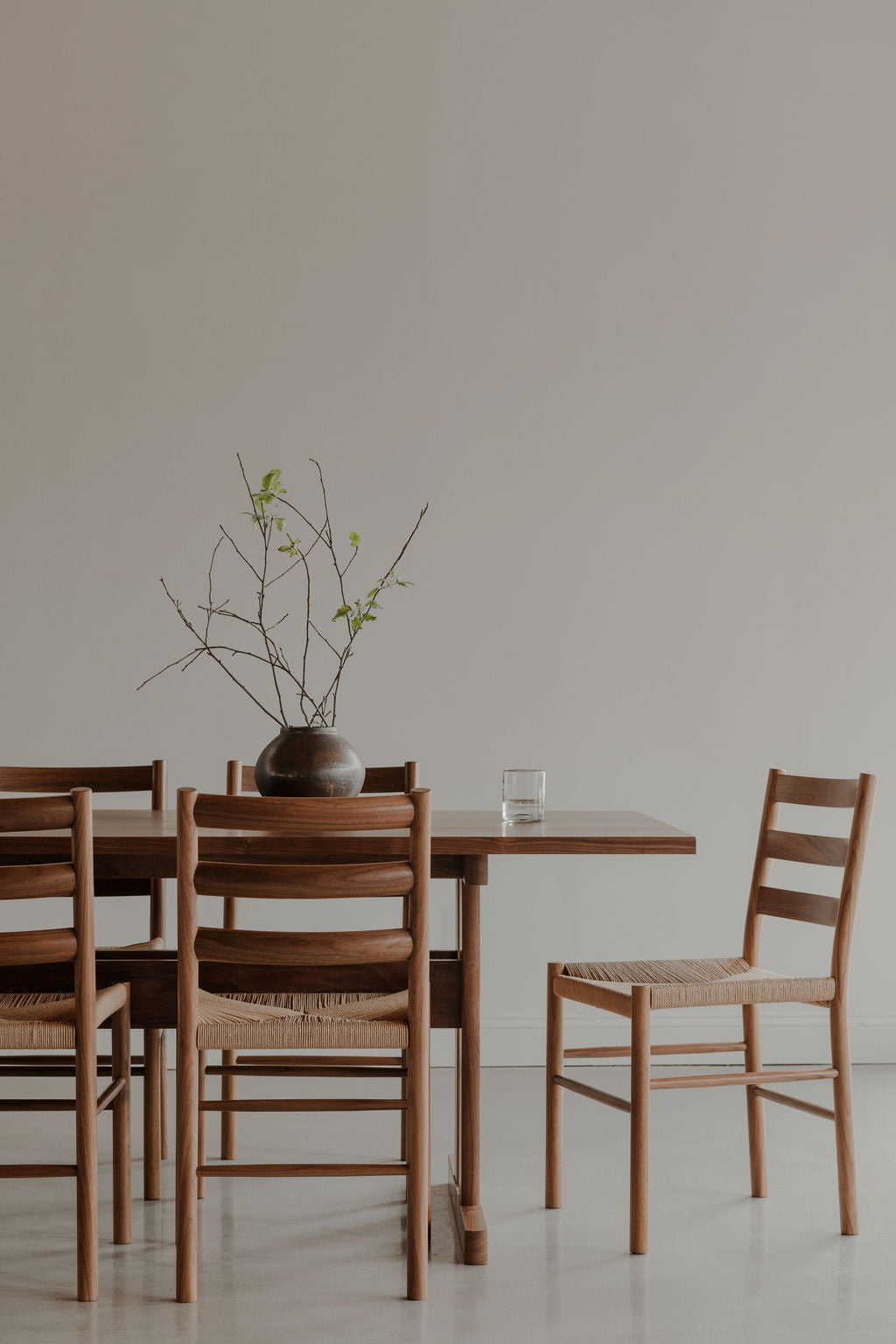 Five Knox Chairs surrounding Knox trestle dining table with glass of water and green plant in vase
