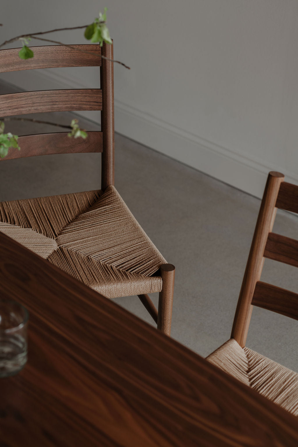 Knox ladder back dining chairs at walnut dining table with glass of water and green plant, photographed artistically at an angle.