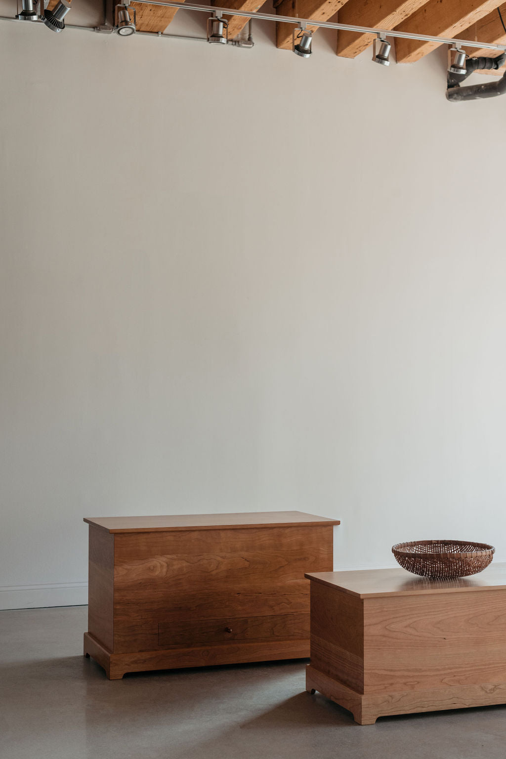 Two wooden blanket chests in a bright open room with wooden beam ceilings