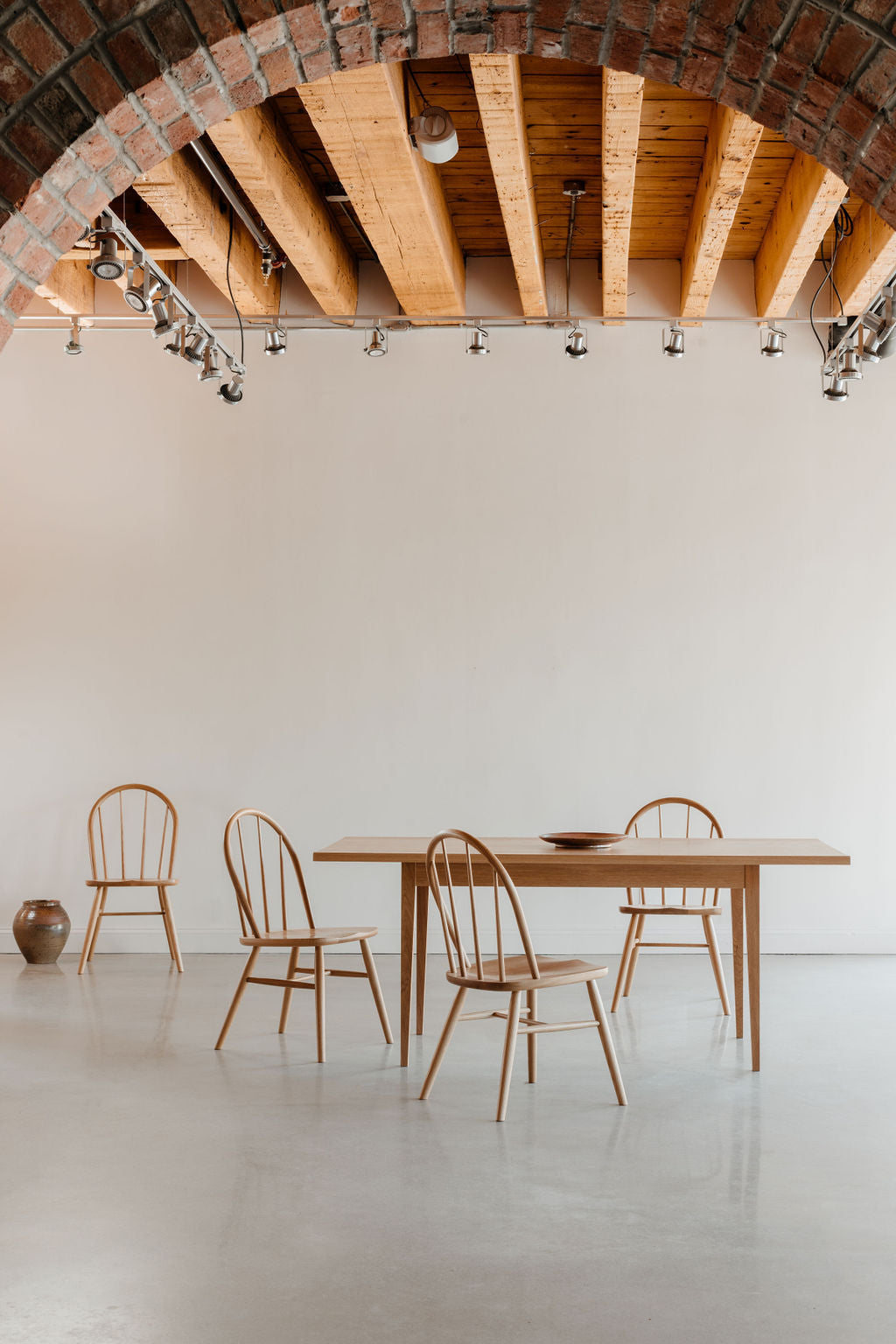 Dining table with four bowback chairs under a brick arch with wooden beams