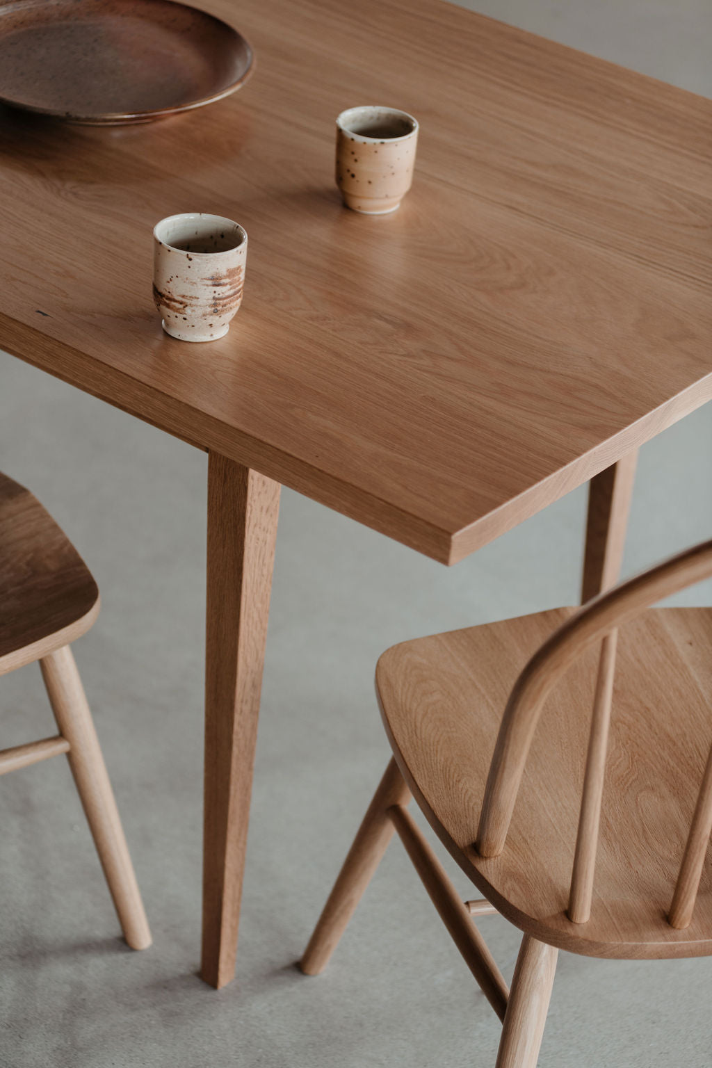 Traditional white oak dining table and bowback chair with ceramic plate and mugs