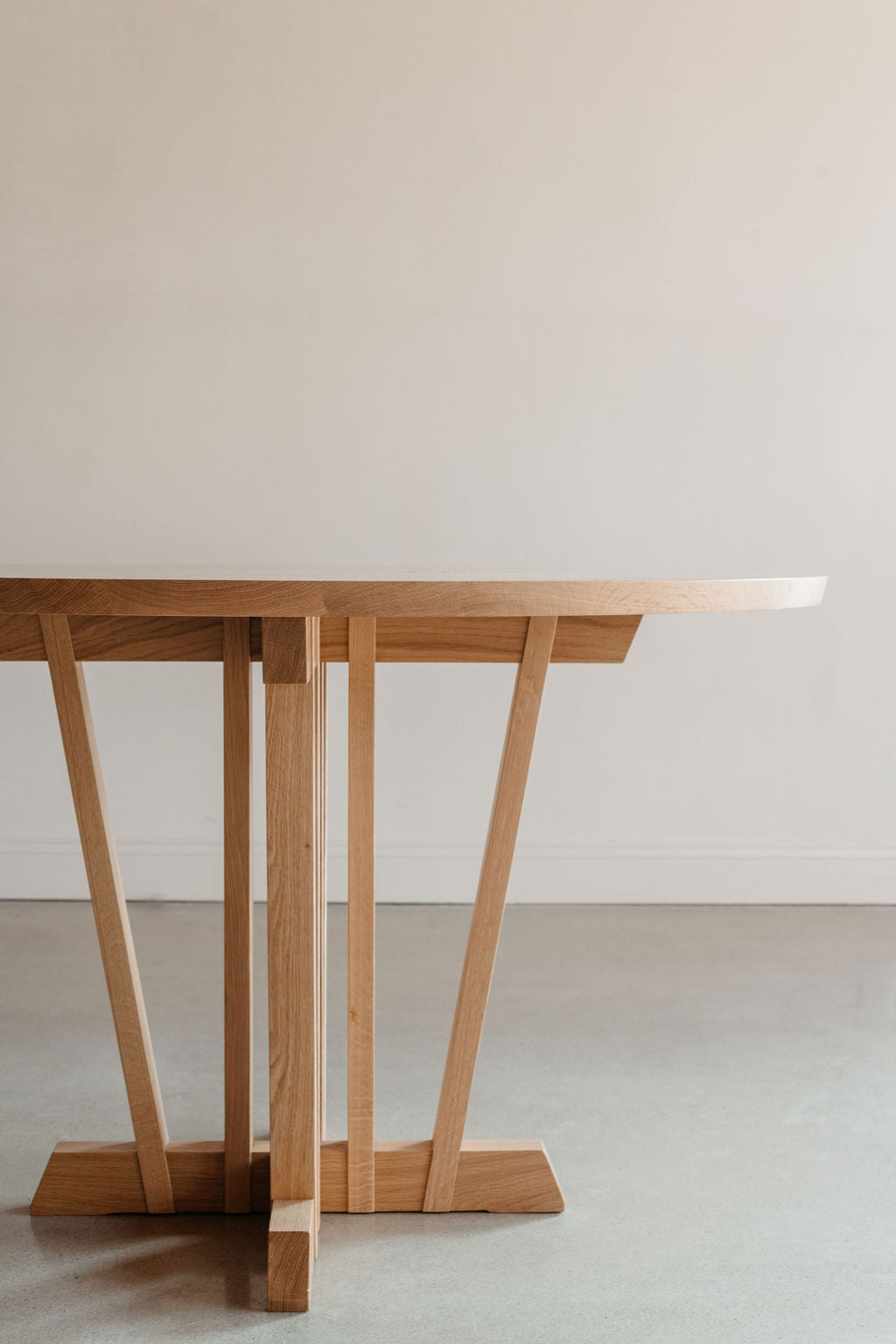 Rigby pedestal dining table in white oak wood in large white room with cement floors.