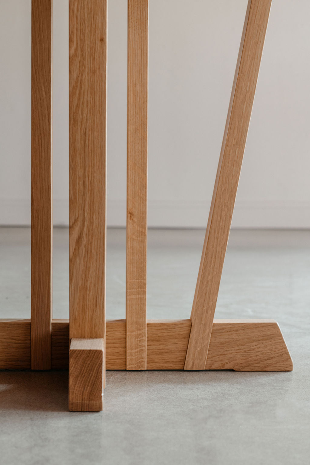 Details of the pedestal base on the Rigby dining table in white oak wood in large white room with cement floors.