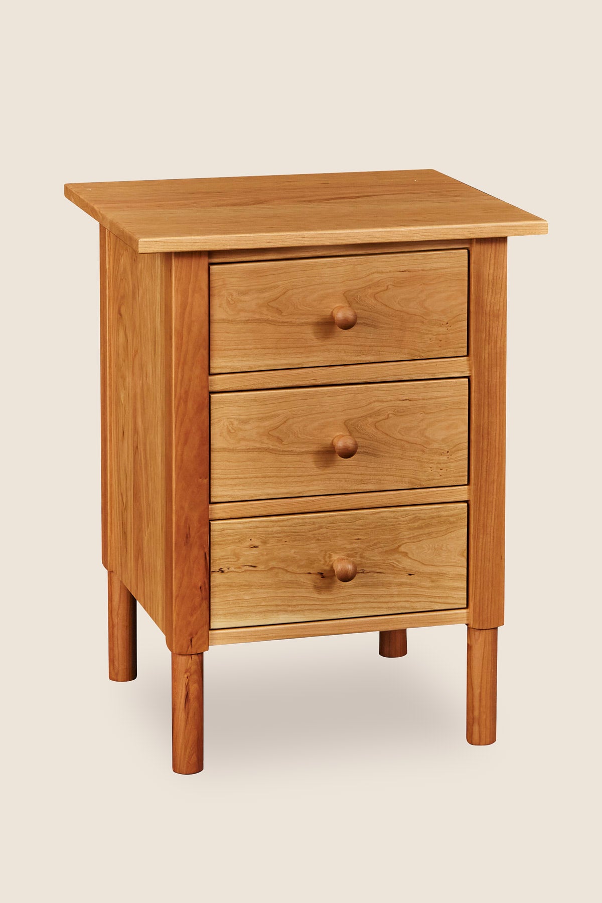 Modern interpretation of a classic Shaker style nightstand with three drawers and rounded legs, in solid cherry wood