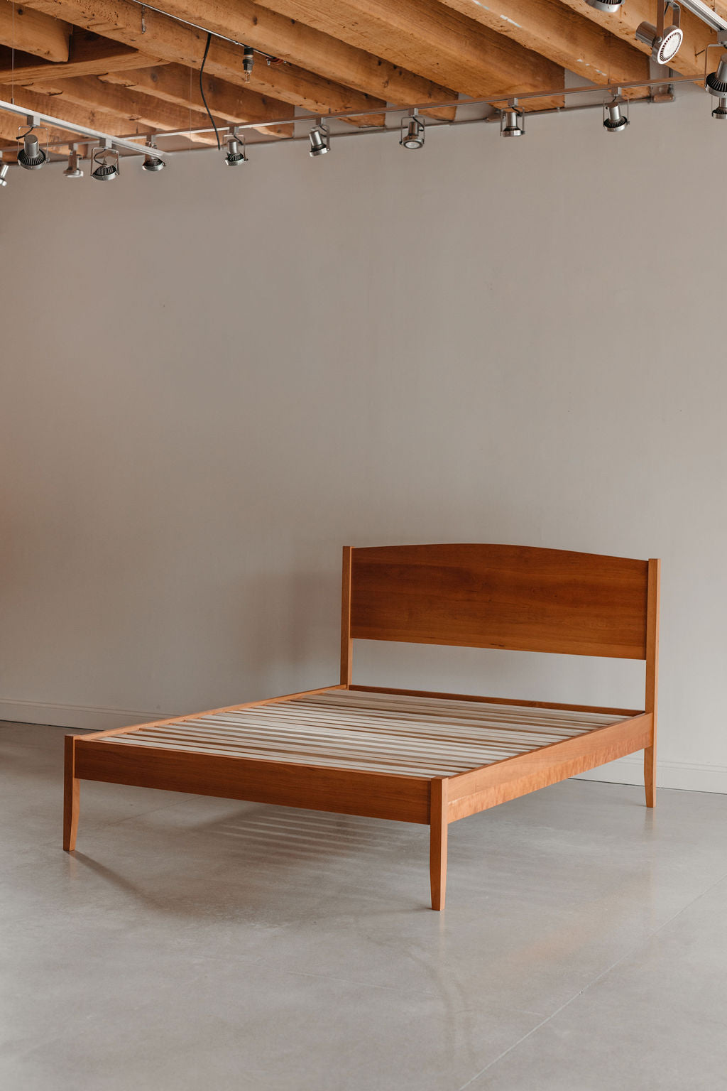 Wooden bed frame against a plain wall with wooden beams on the ceiling.