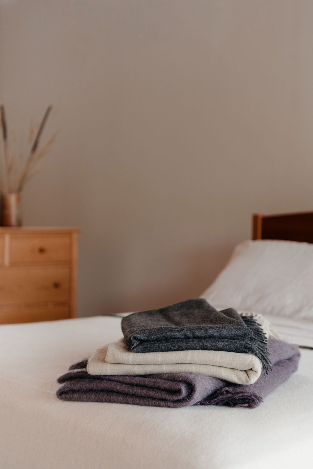 Stack of folded blankets on a bed with a neutral background