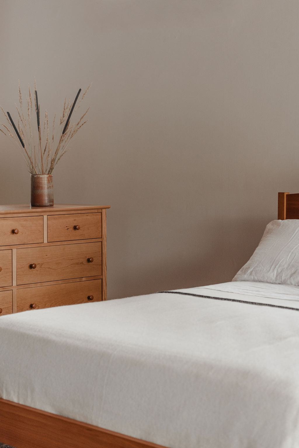 Bedroom with wooden dresser and bed against a beige wall