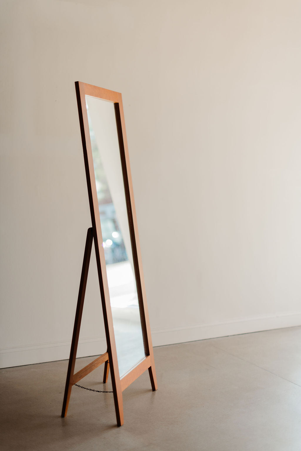 Wooden-framed self-standing mirror in front of a plain wall.