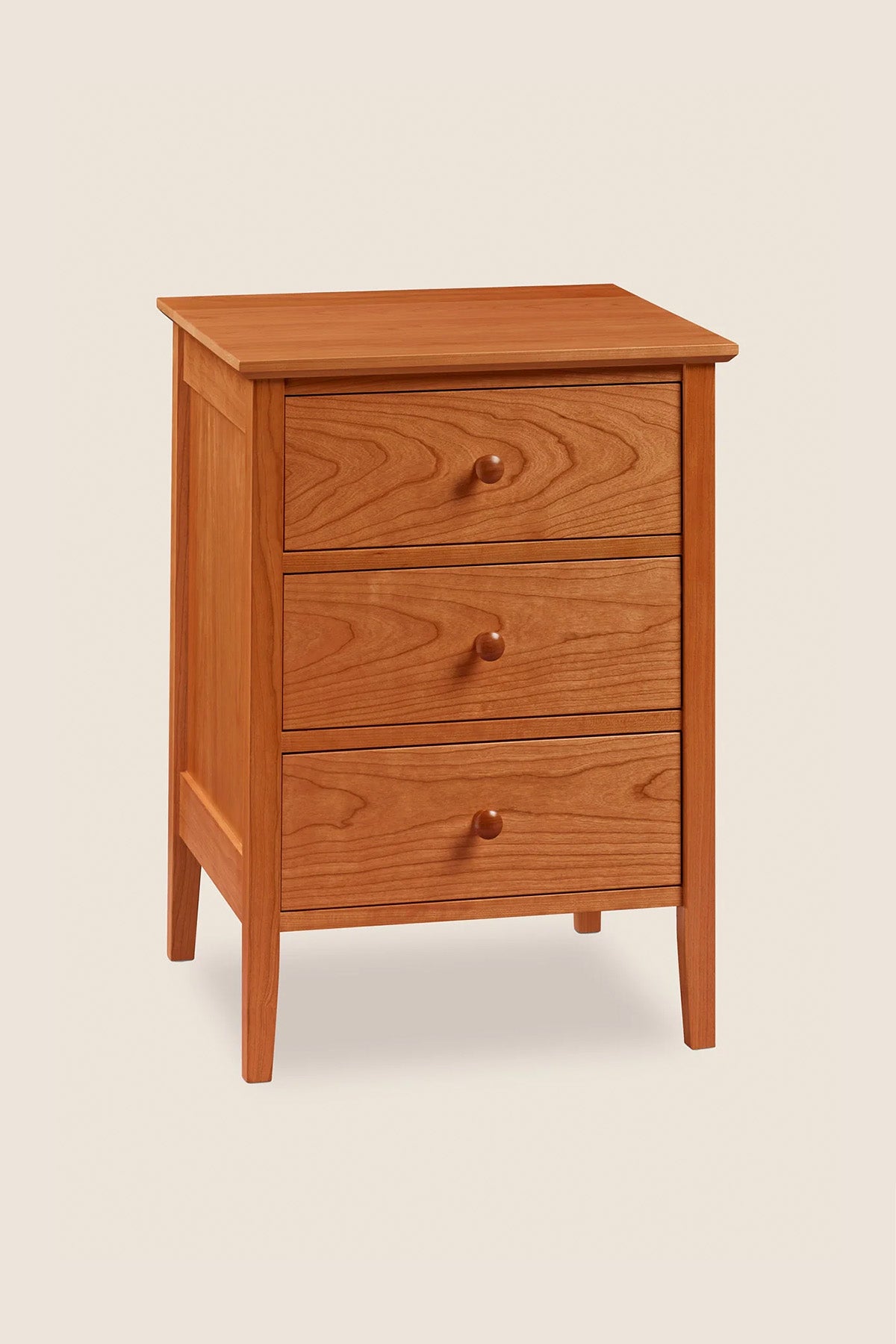 Simple Shaker nightstand with three drawers and tapered legs, in cherry wood, from Maine's Chilton Furniture Co.