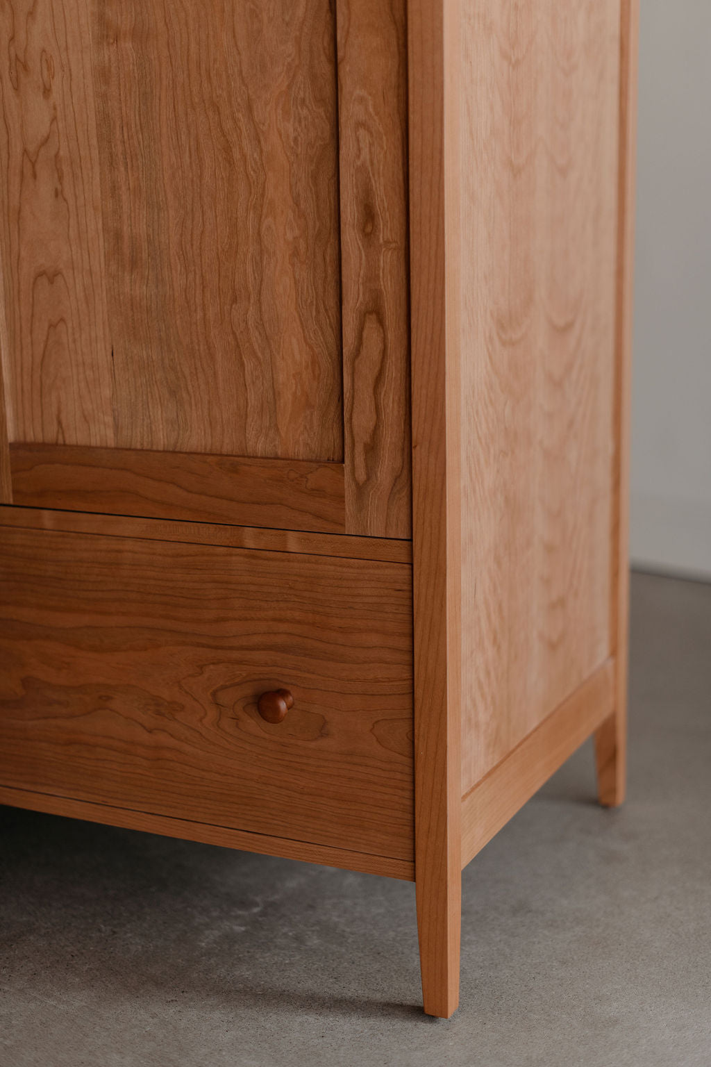 Wooden Shaker wardrobe cabinet with a drawer and knob on a gray floor.