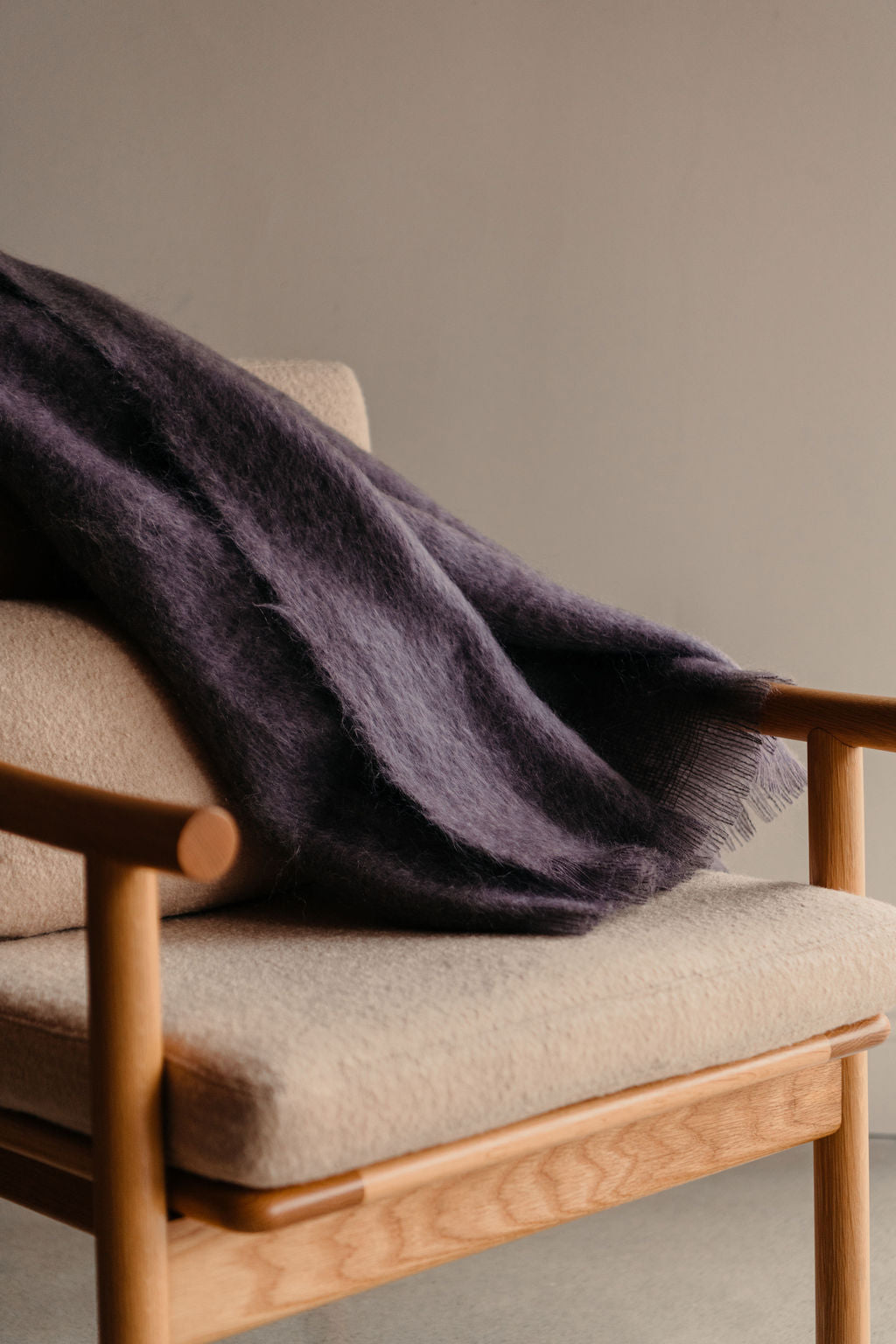 Beige armchair with a purple mohair throw blanket draped over it against a plain wall.