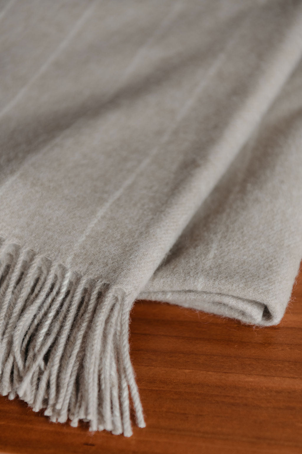 Gray merino throw blanket with fringes on a wooden surface