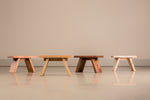 Line up of four angular milking stools in cherry, white oak, walnut and maple, from left to right