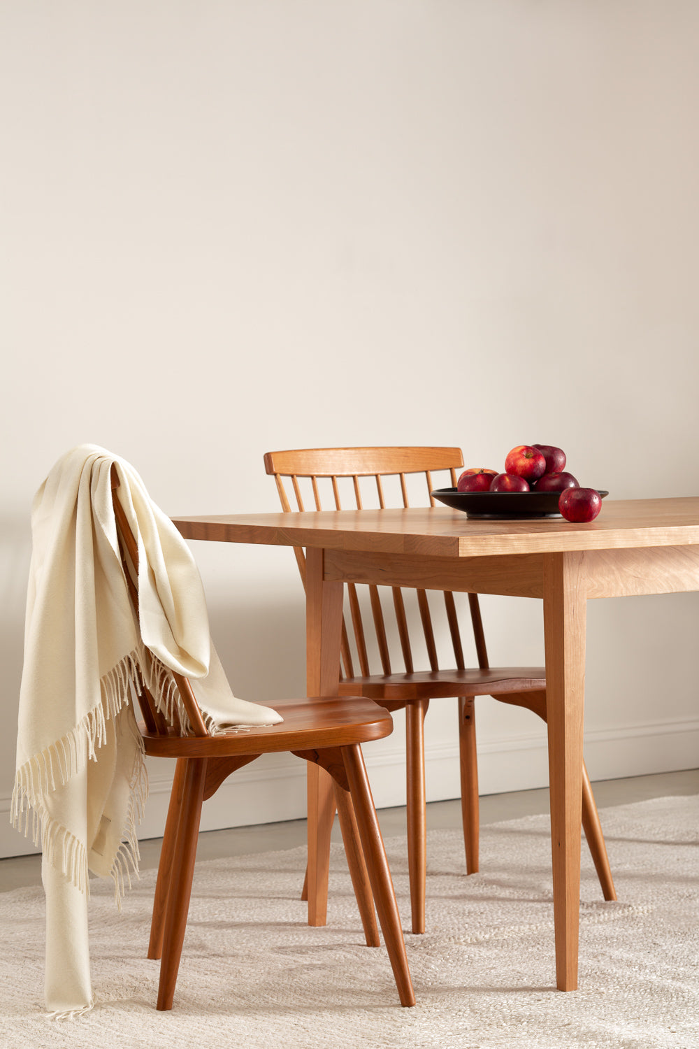 Two Chilton Spindle Chairs with the Shaker Heirloom Dining Table in cherry styled with a white blanket throw and a bowl of red apples.