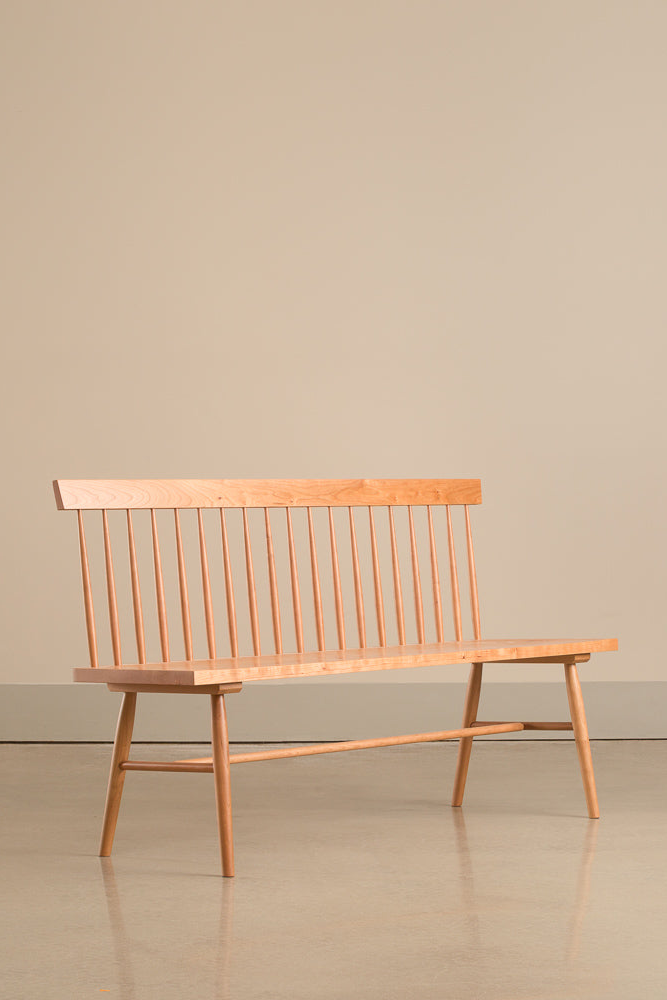 A side view of the Broadside spindle back bench in a tan room with cement floors