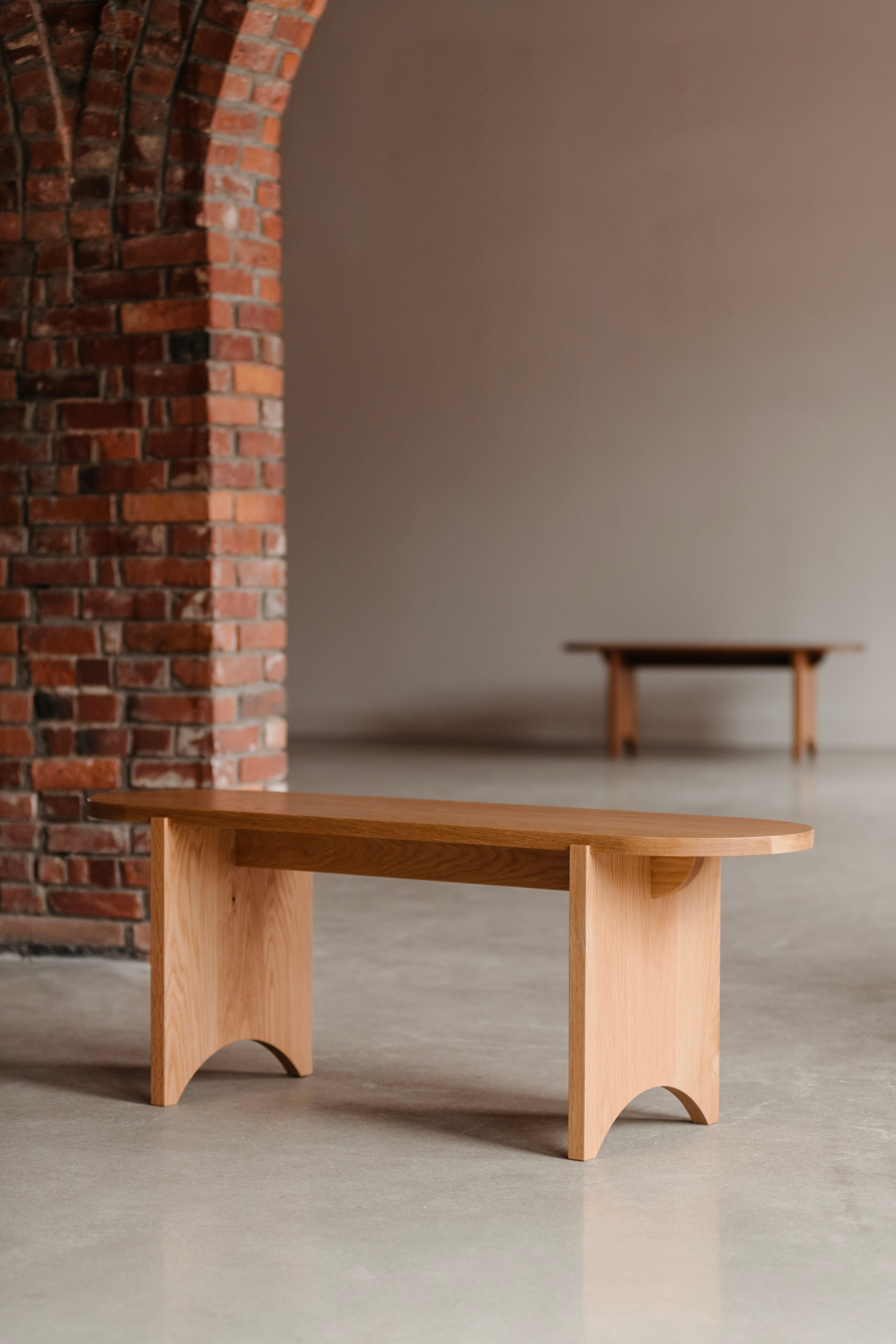 Modern Shaker inspired bench in white oak in minimalist setting with brick arch to the left and walnut bench in background.