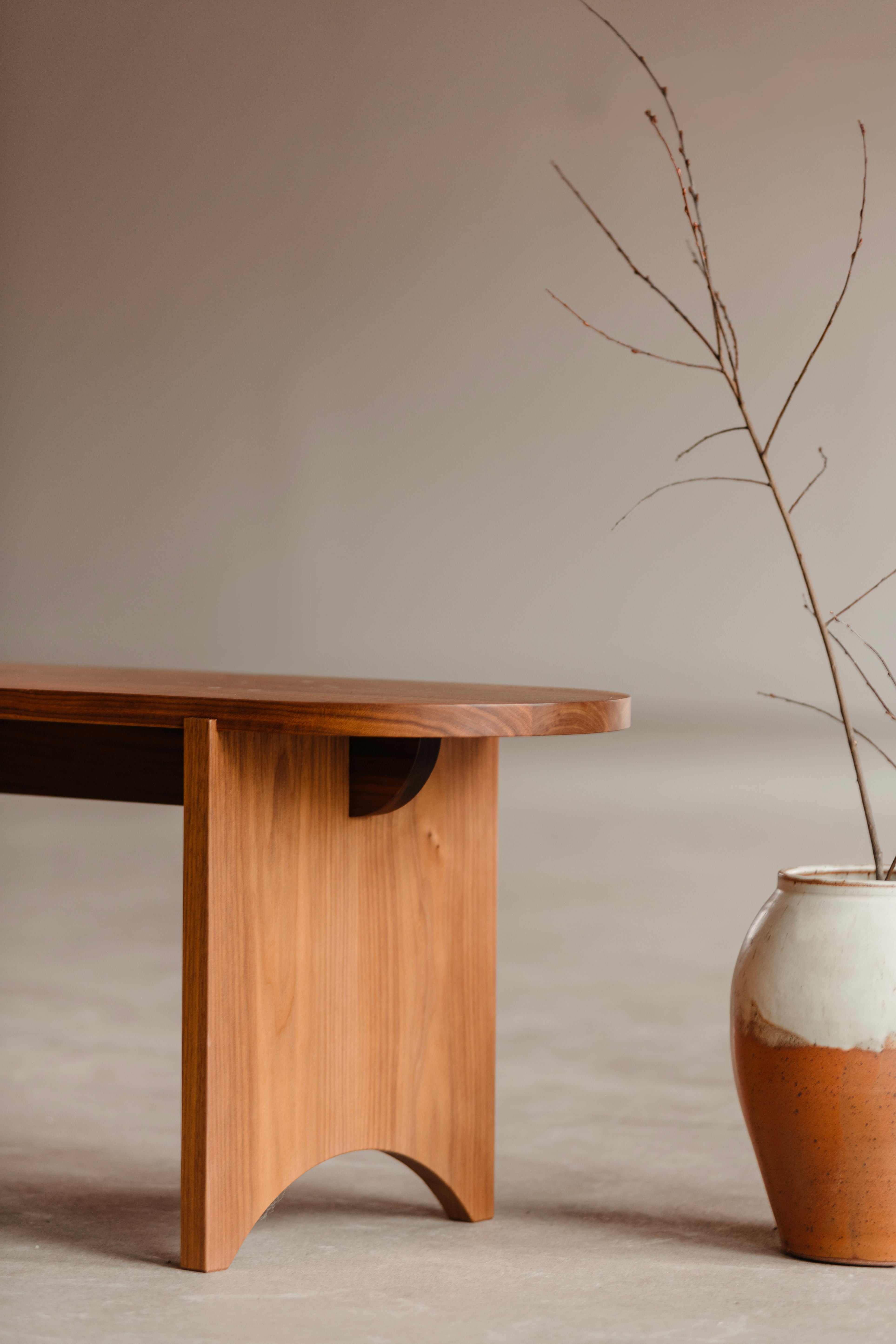 Modern Shaker walnut bench with rounded edges and legs from Chilton Furniture in Maine accompanied by large hand thrown vase.