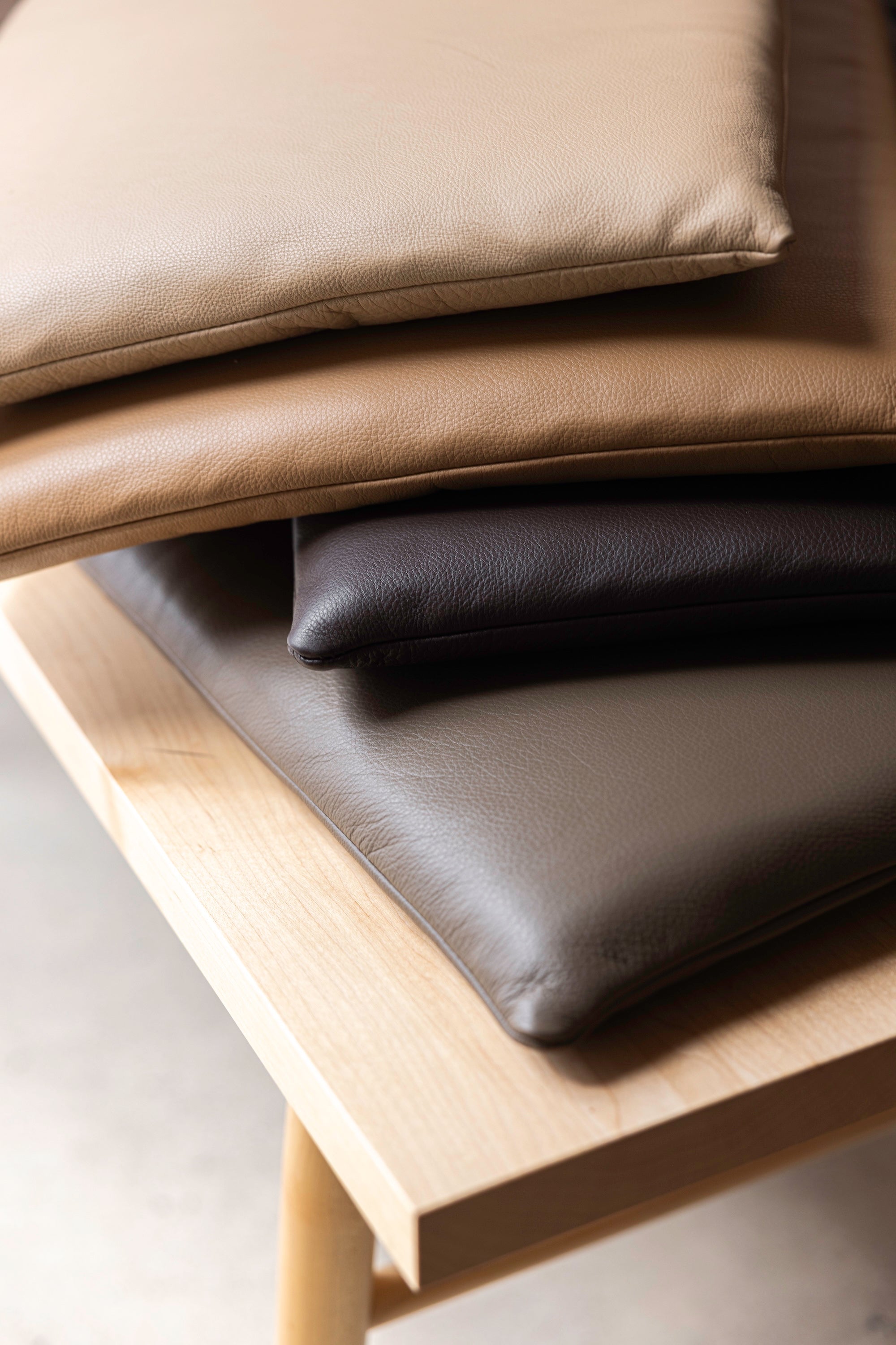 Four leather cushions in multiple shades of brown stacked on a solid maple bench