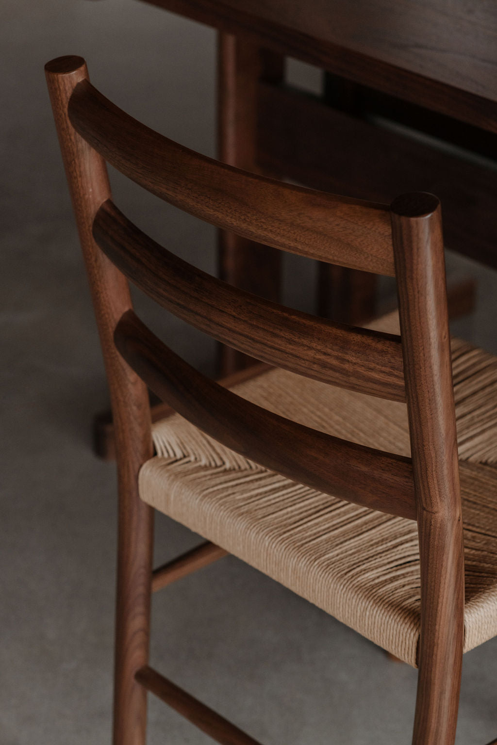 Rounded backrest rungs meet cylindrical post legs on walnut Knox dining chair with woven danish cord seat