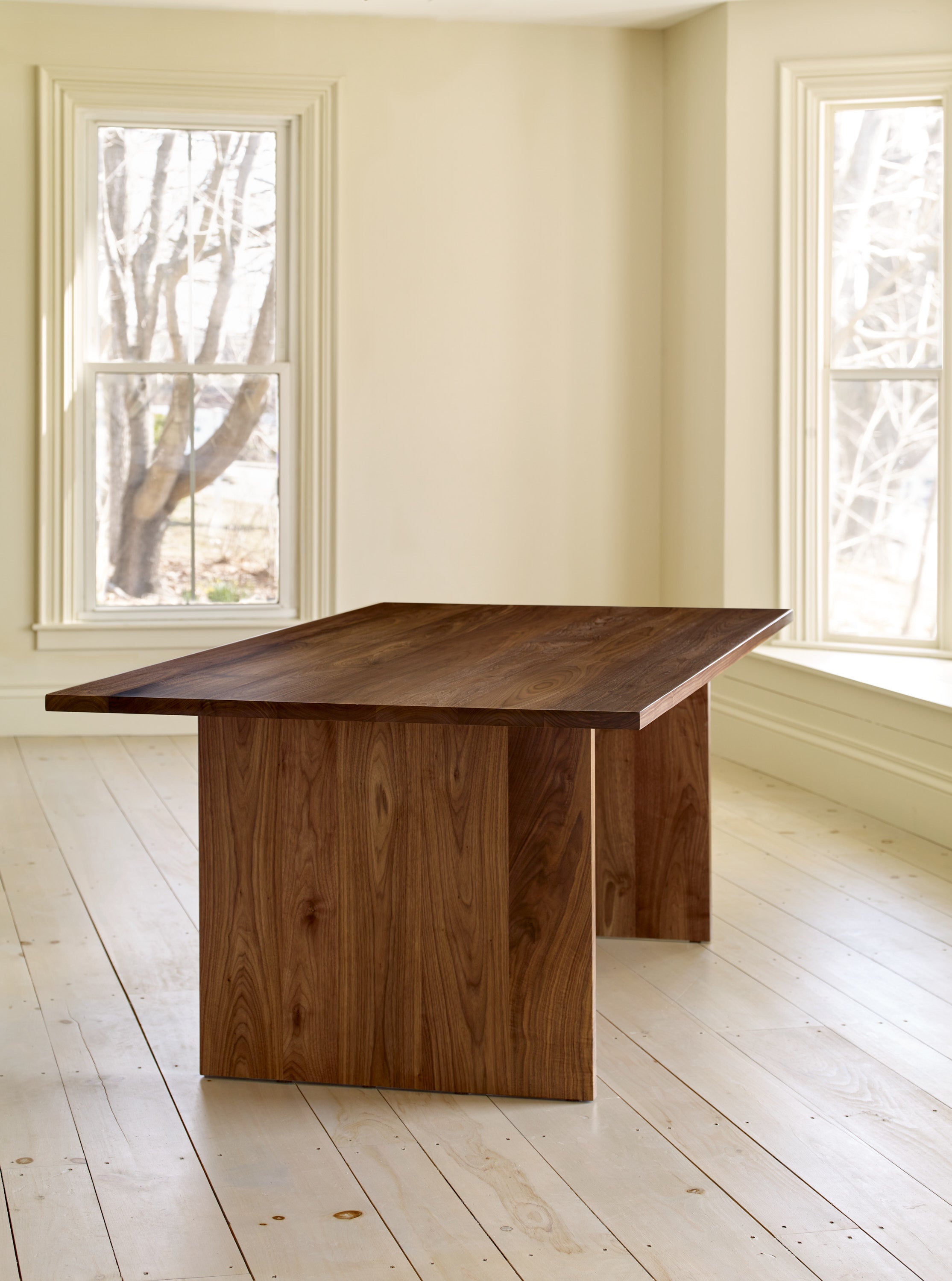 Walnut trestle style Hygge Dining Table in bright window lit room on wood pine floors