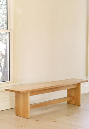 Modern trestle style Hygge Bench in white oak in bright room along wall with windows