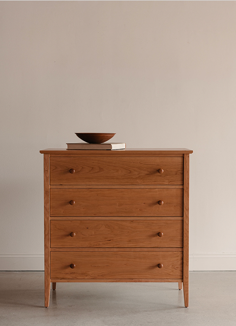 Wooden dresser with four drawers styled with a book and wooden bowl on a plain background