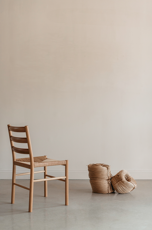 Wooden chair with woven seat and rolls of paper cord against a plain wall