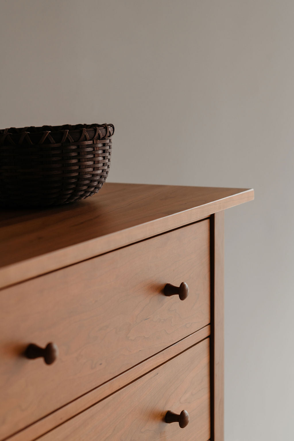 Wooden dresser with wicker basket on top against a plain wall