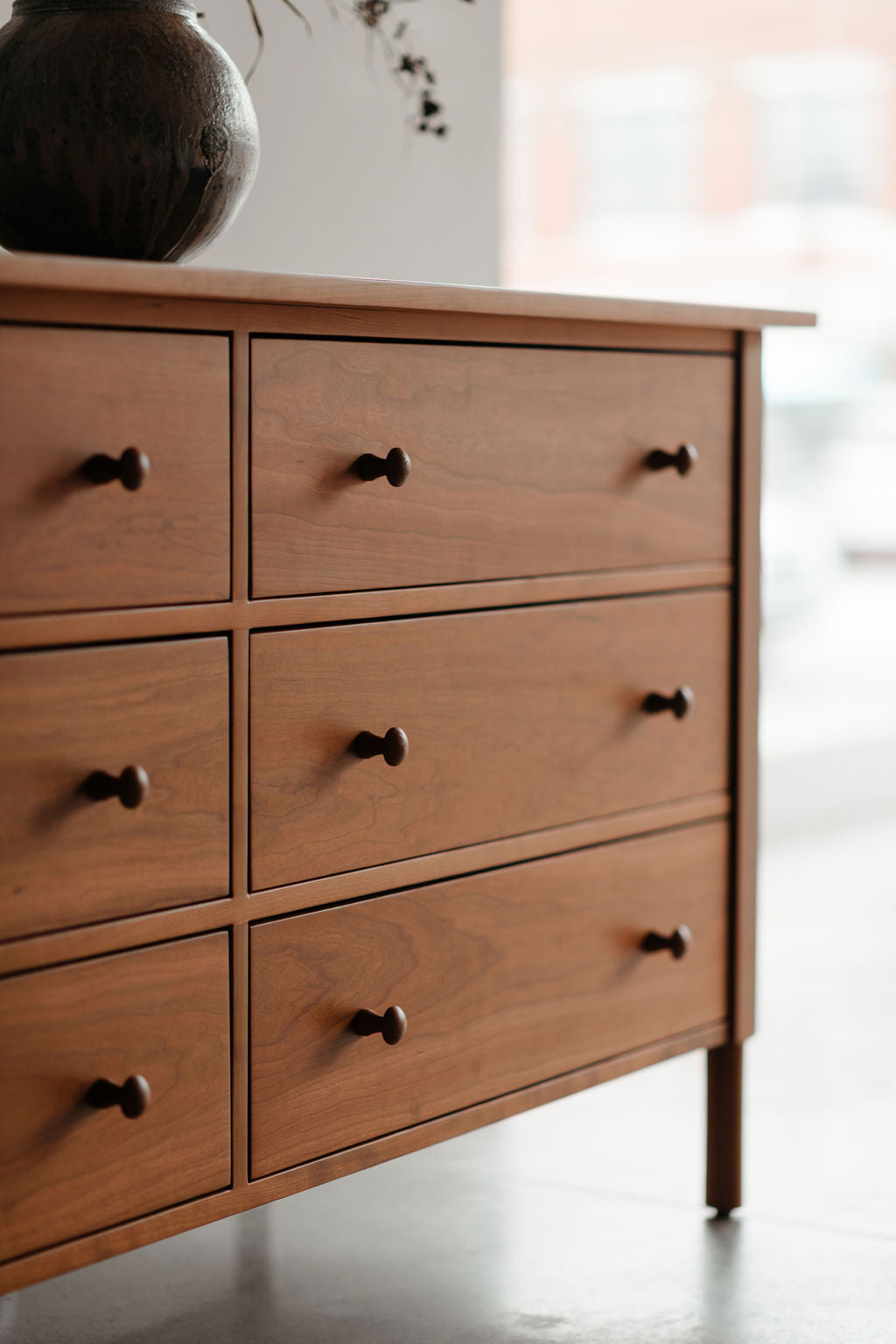 Wooden dresser with six drawers and mushroom style knobs on a blurred background