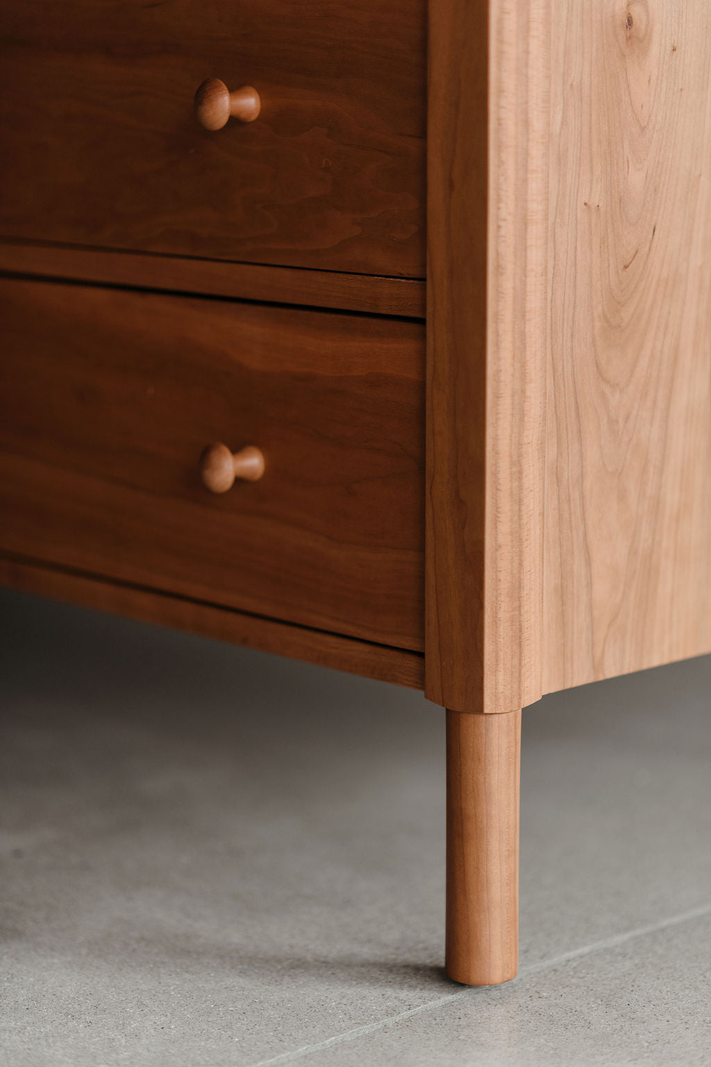 Wooden dresser with rounded legs on a gray floor.