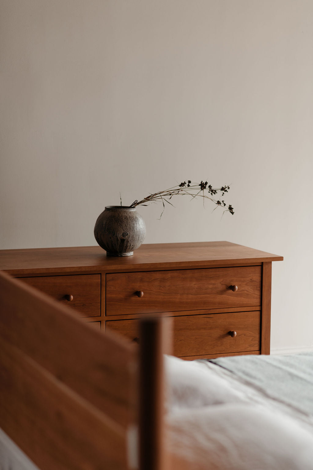 Wooden dresser with a vase and branches against a plain wall