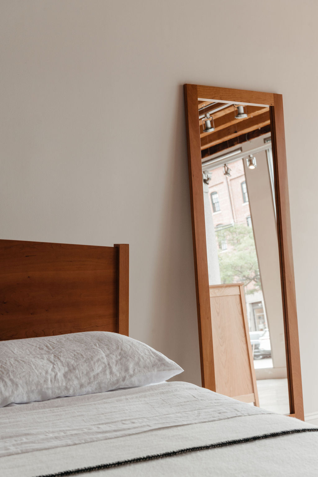 Wooden Shaker style headboard next to a mirror on a white wall