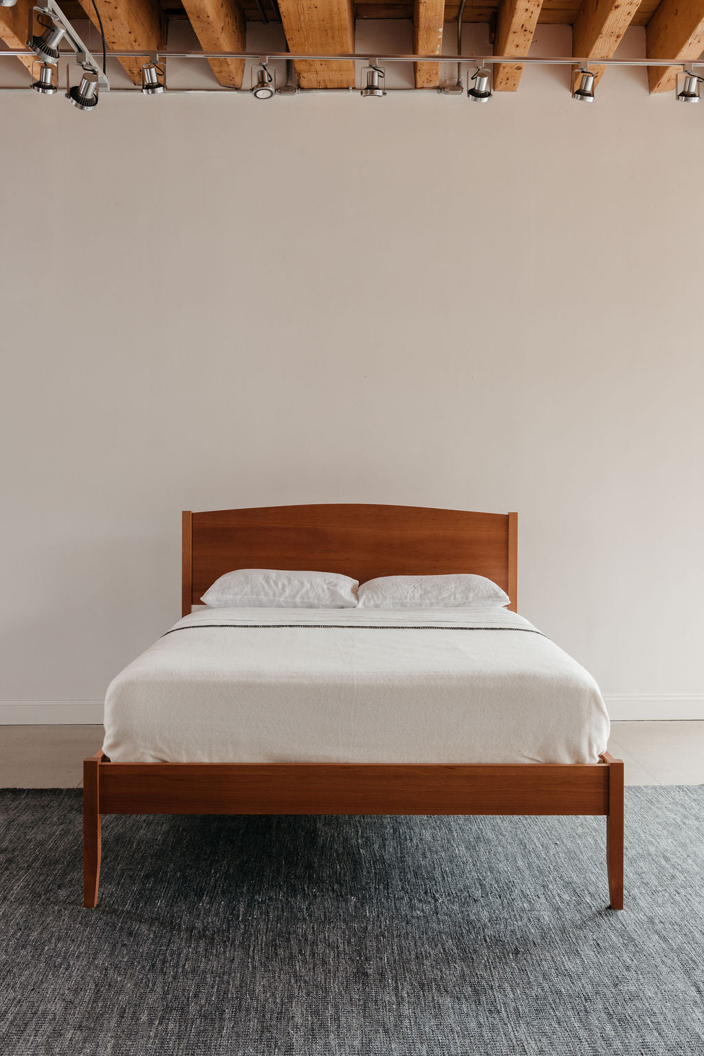 Wooden Shaker bed with white bedding against a plain wall