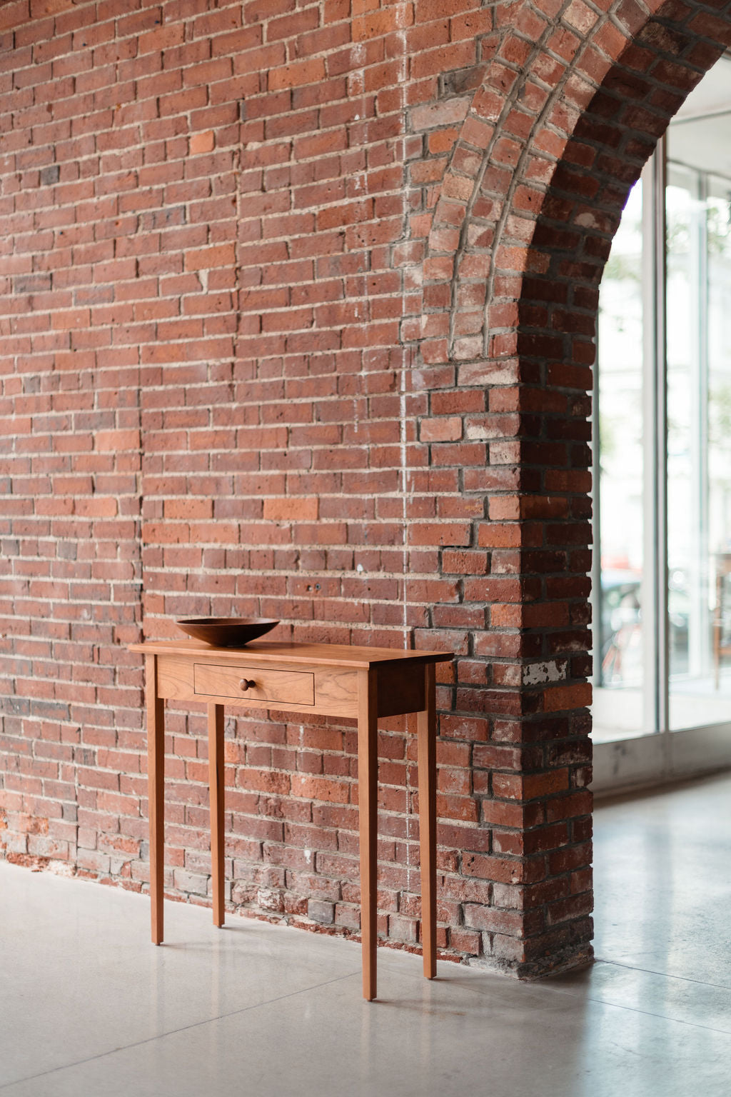 Wooden Shaker style table against a brick wall with large windows in the background