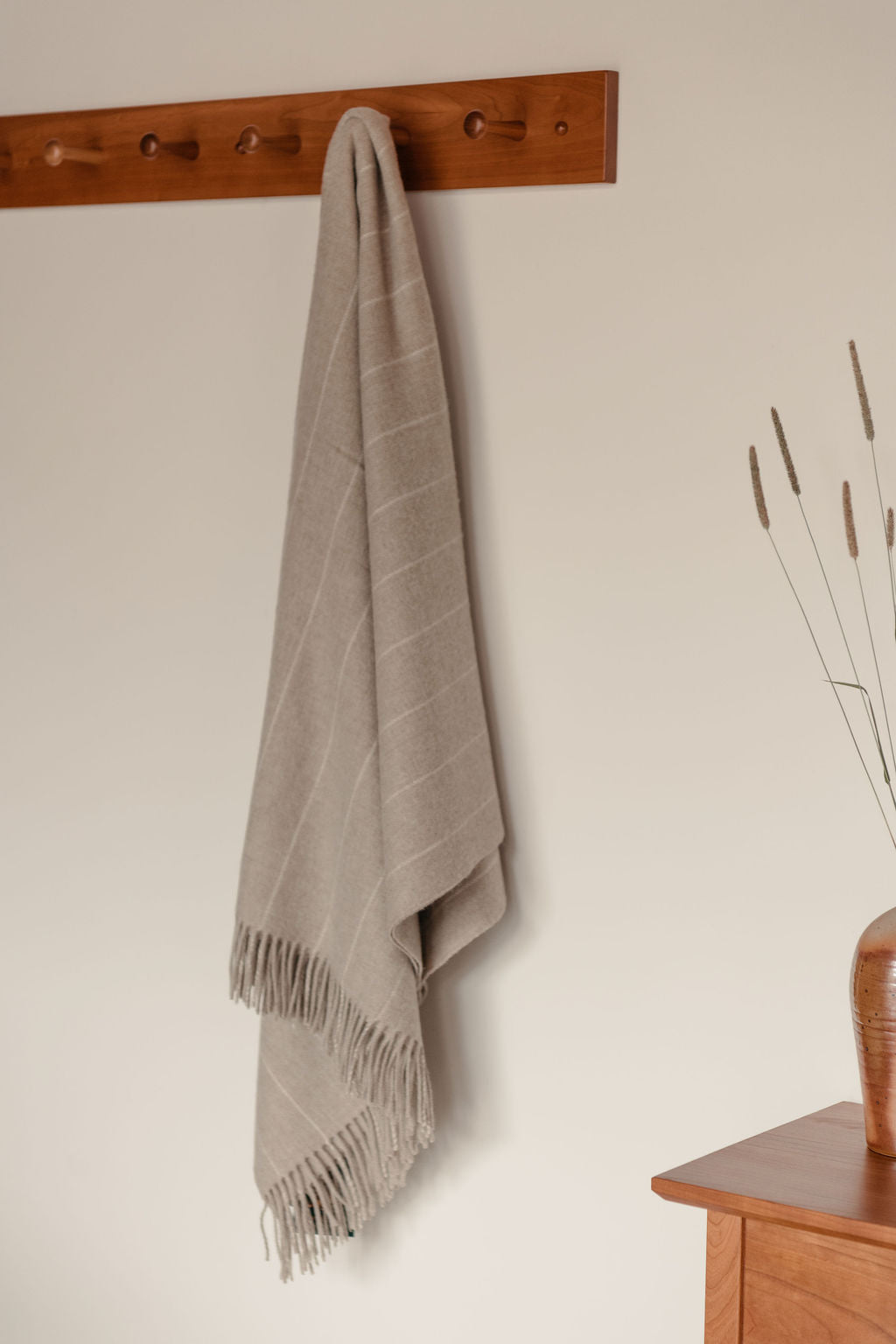 Gray throw blanket hanging on a wooden peg rack against a beige wall.