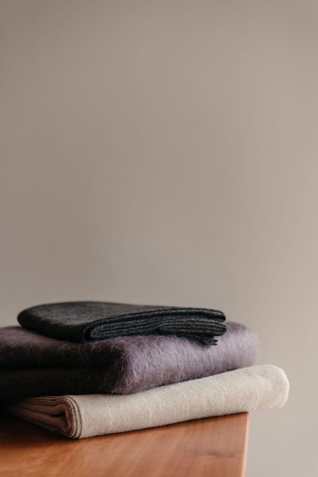 Stack of folded soft woven throw blanket on a wooden surface with a neutral background