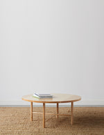 Round, maple wood, Scandinavian inspired coffee table with round legs on beige woven rug with table top magazines and white background