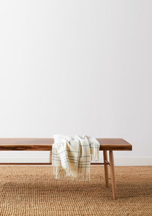 Walnut live edge bench with cream checkered throw blanket on beige woven rug